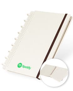 cade do disco ecológico com design vintage de cor marrom e amarela, feito de material reciclado. O caderno está aberto mostrando folhas em branco e uma caneta ao lado. No fundo, há um laptop e um livro, indicando um ambiente de escritório.